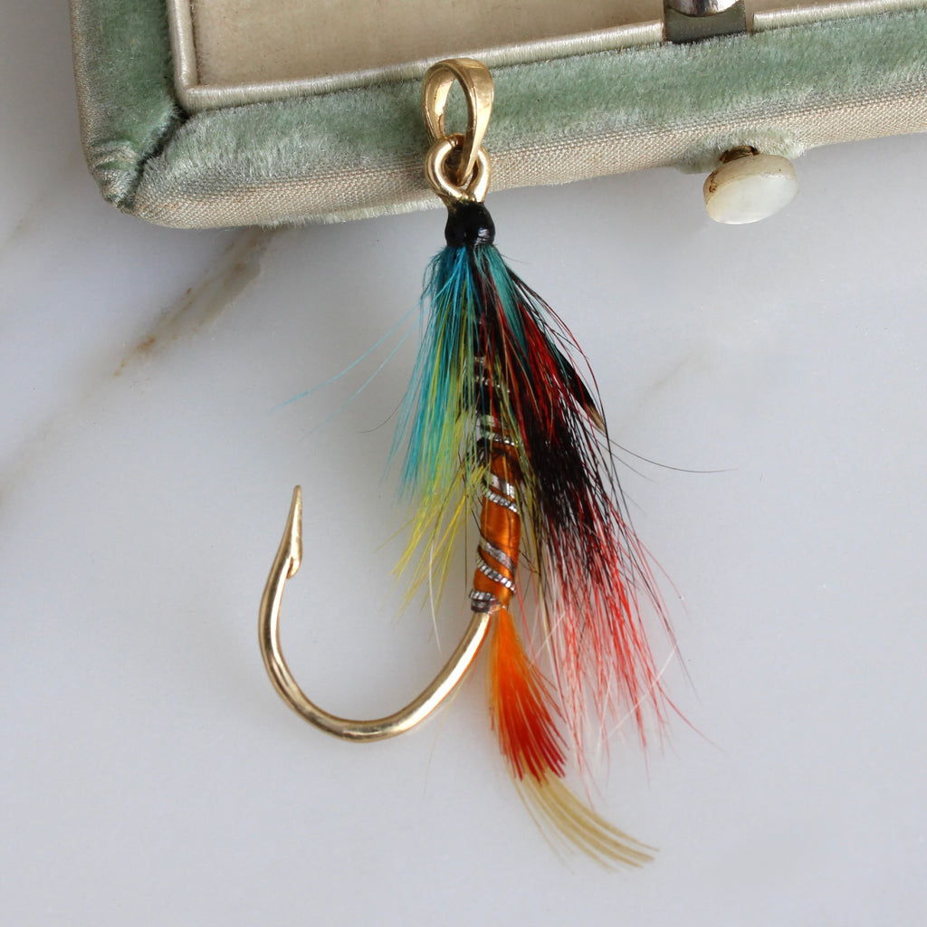 a solid yellow gold fish hook tied with colorful feathers as a pendant 