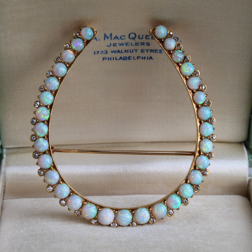 large horseshoe shaped brooch in yellow gold with round opals and diamond set along the edge