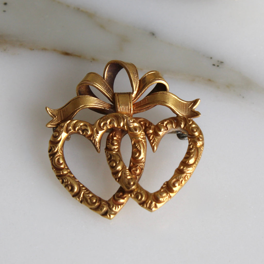 brooch of two gold linked hearts with a bow on top