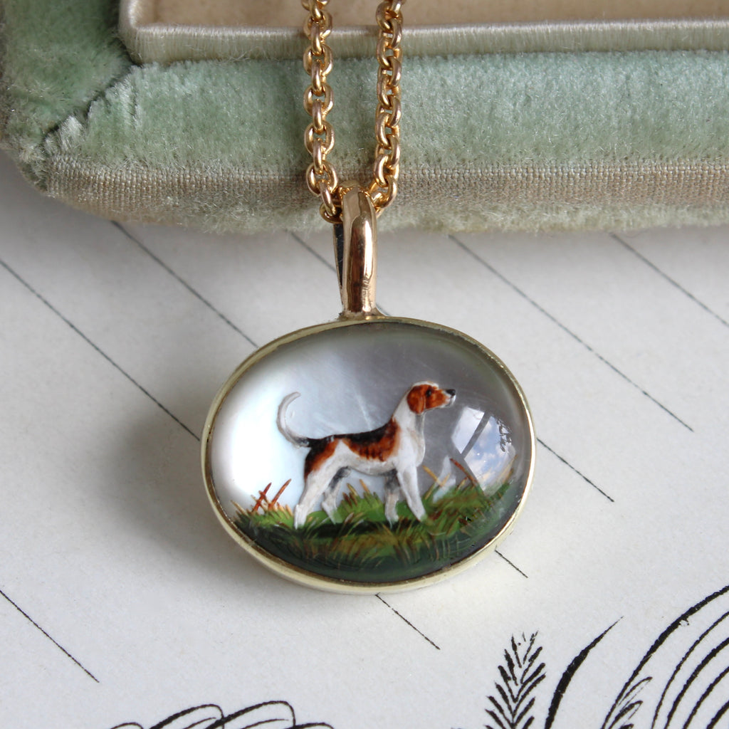 a gold pendant set with a crystal cabochon that shows a hound or beagle realistically painted, hung on a gold chain