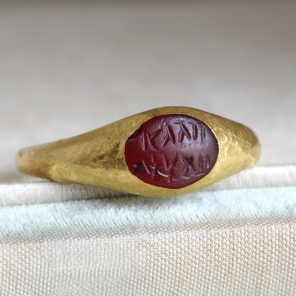yellow gold ring with an oval red stone engraved with greek letters