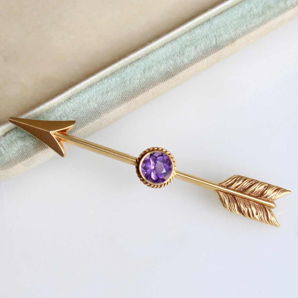 gold brooch that looks like an arrow shot through a round purple gemstone