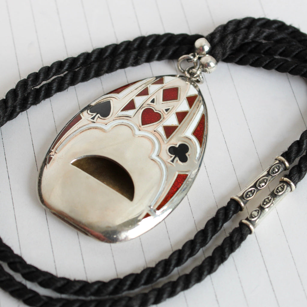 large silver whistle with red black and white enamel playing card motif hung on blcak cord as a pendant