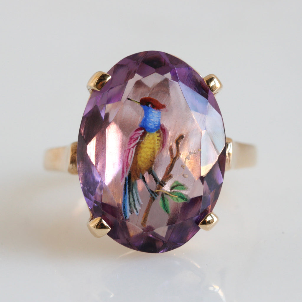yellow gold ring with large purple stone painted with a colorful bird