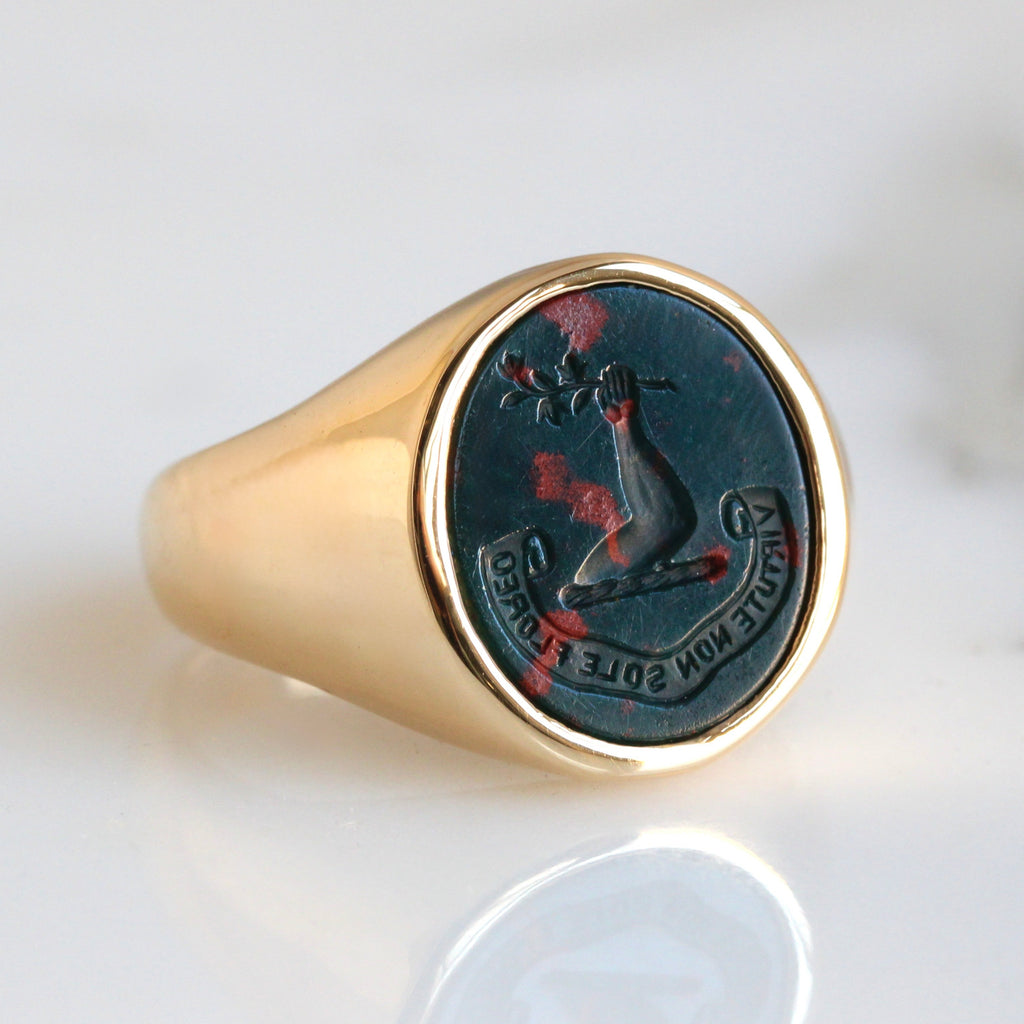 yellow gold signet ring with oval bloodstone face carved with a raised arm holding a flower branch.