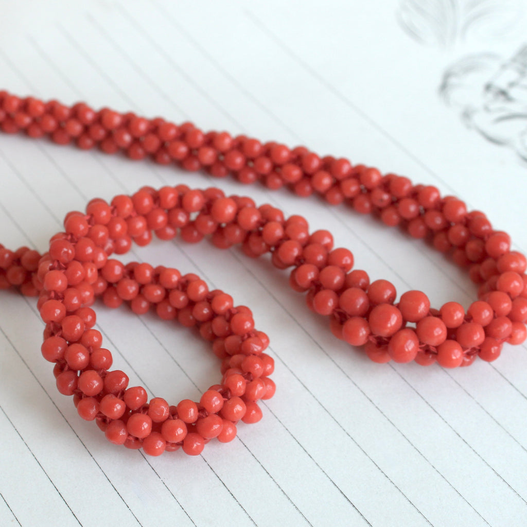 a necklace of red coral beads woven as a tube strand on coral silk