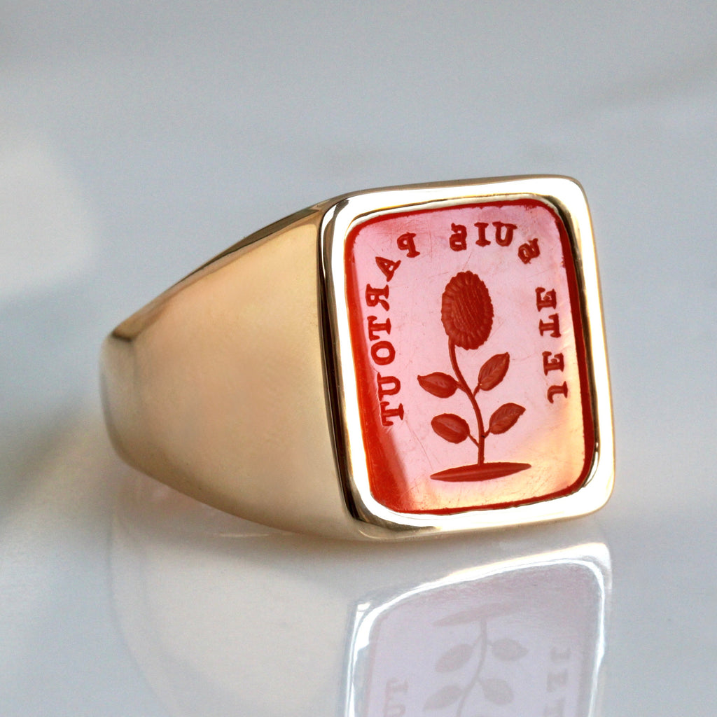 yellow gold ring with inlaid face of orange stone carved with french words and a flower