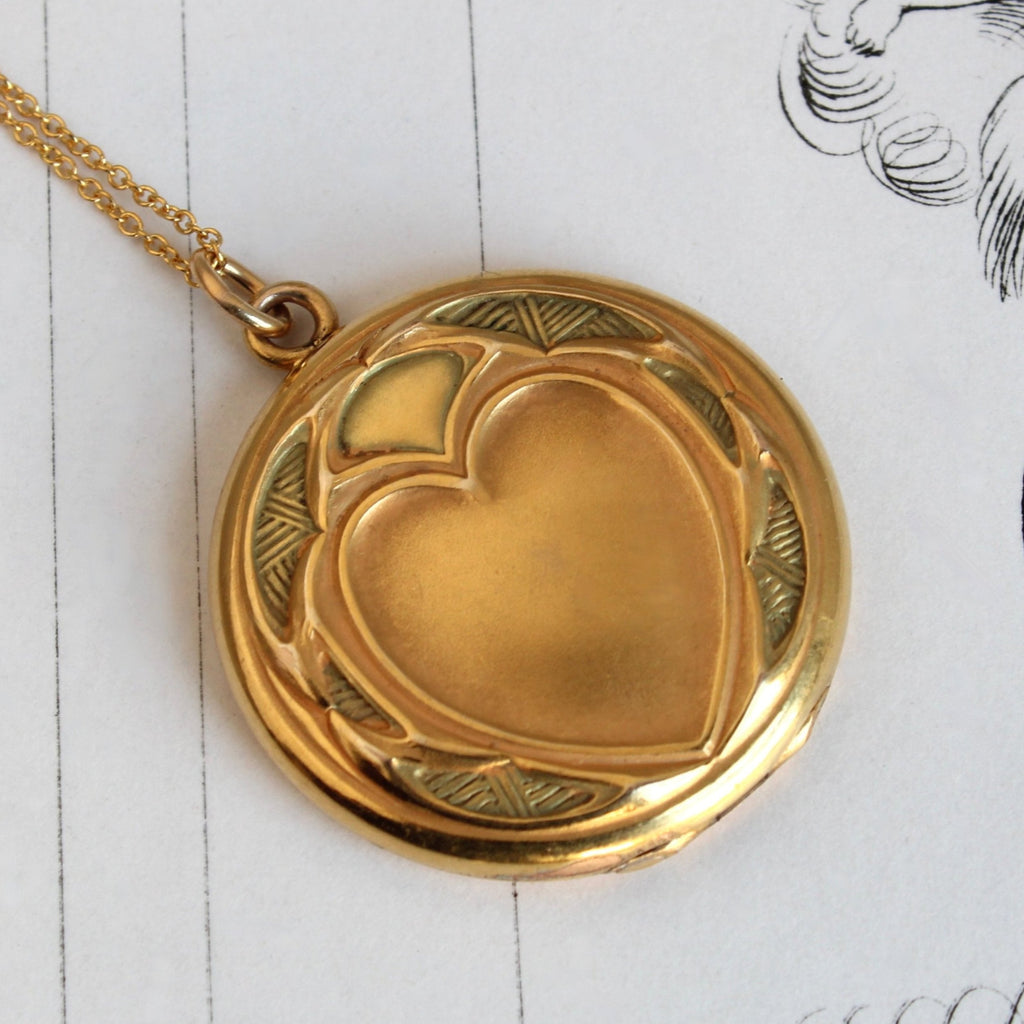 antique round locket in gold metal with a heart embossed on the front cover on a gold chain