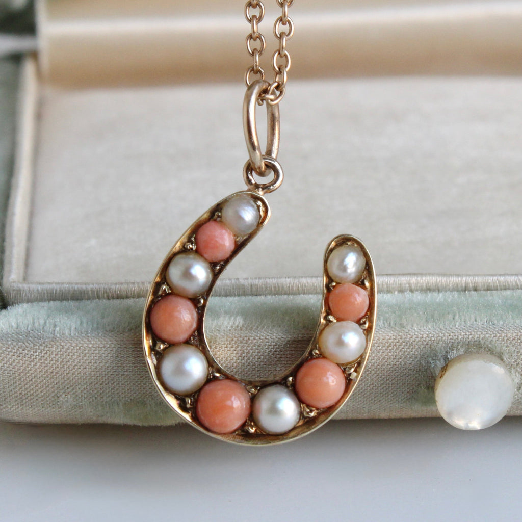 gold horseshoe-shaped pendant with pearls and peach-colored beads on a chain