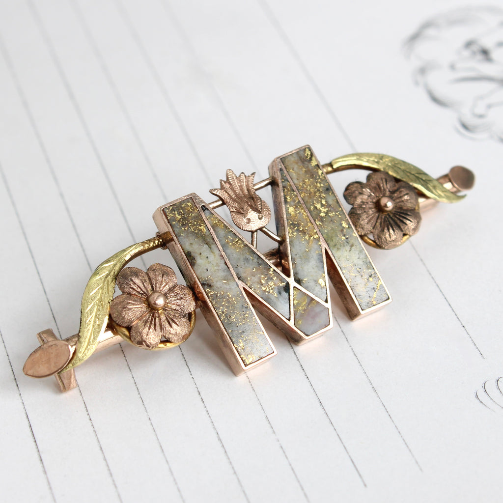 rose gold brooch with the initial M set with marble quartz that has pure gold veins running through it