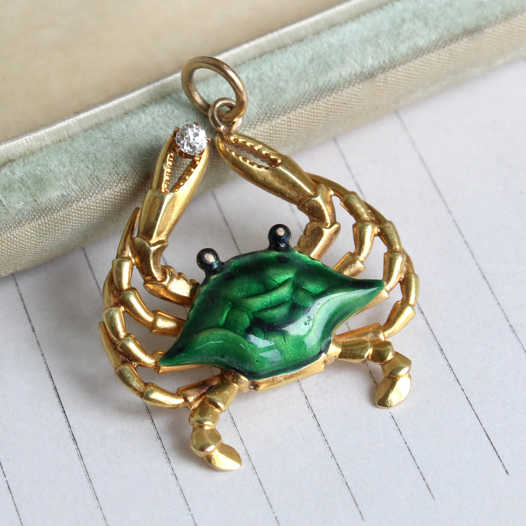 yellow gold crab with realistic details and a green enamel shell, holding a small diamond in one claw.