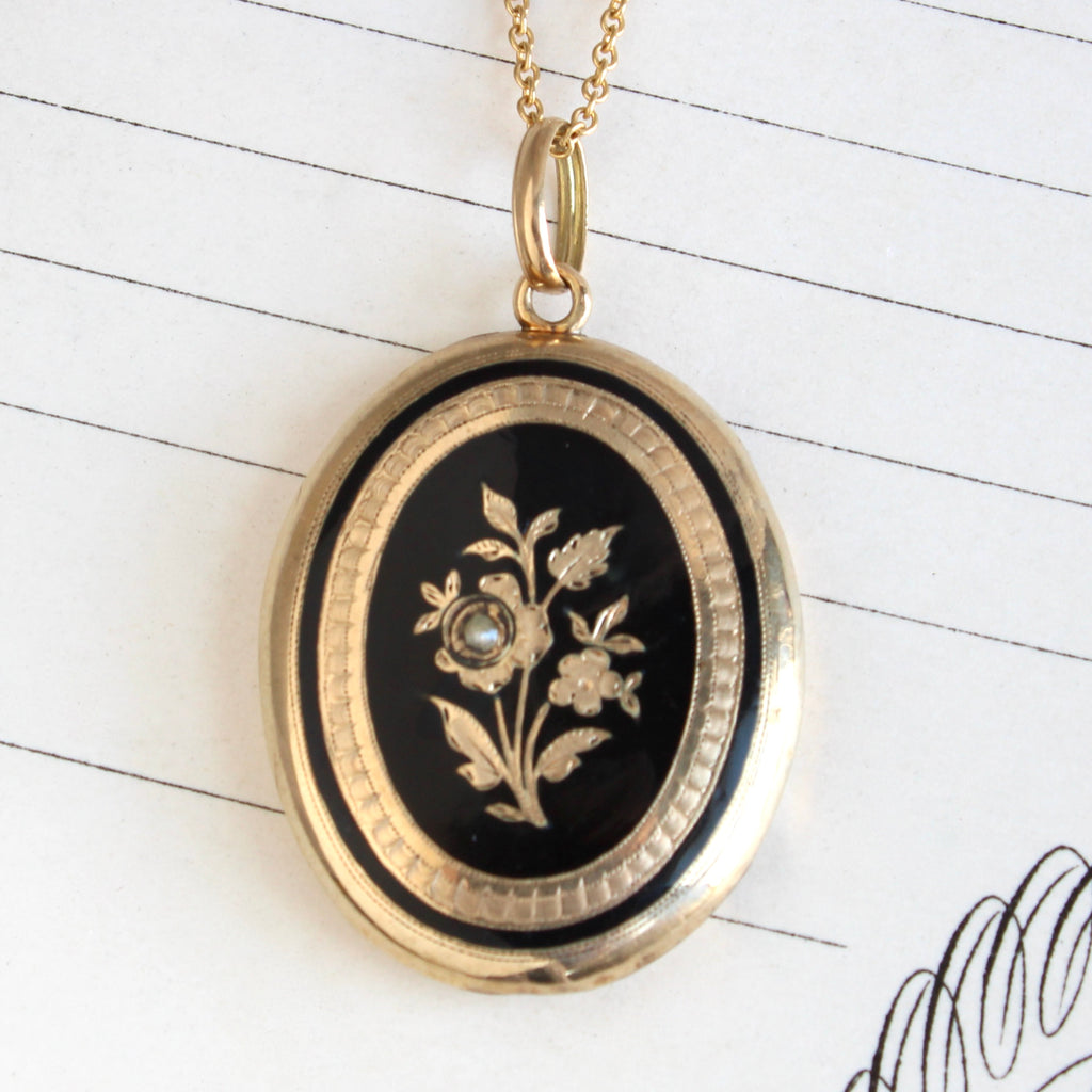 gold locket with a spray of flowers on the front outlined in black enamel, on a gold chain
