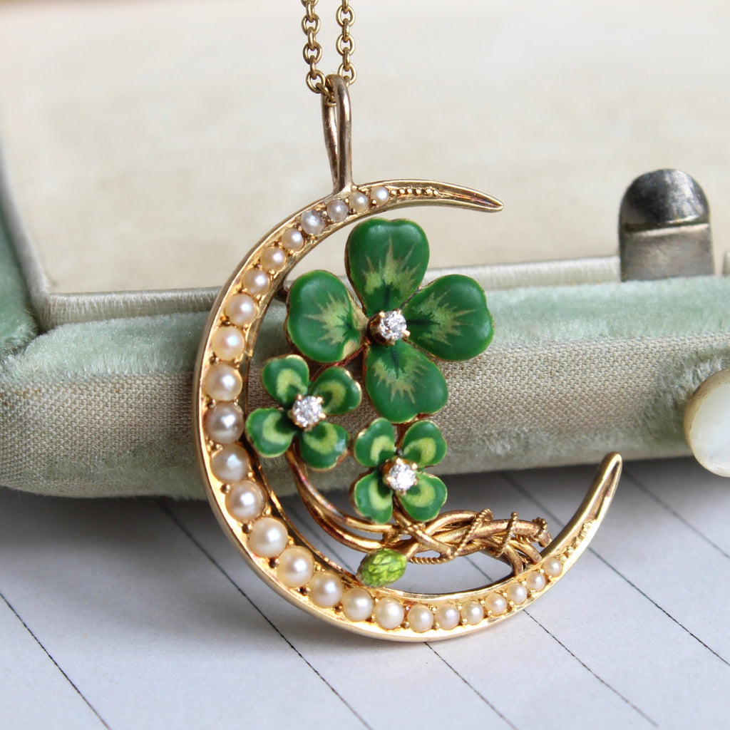 pendant with yellow gold crescent set with seed pearls framing three green enameled four leaf clovers, each with a diamond in the center. on a gold chain