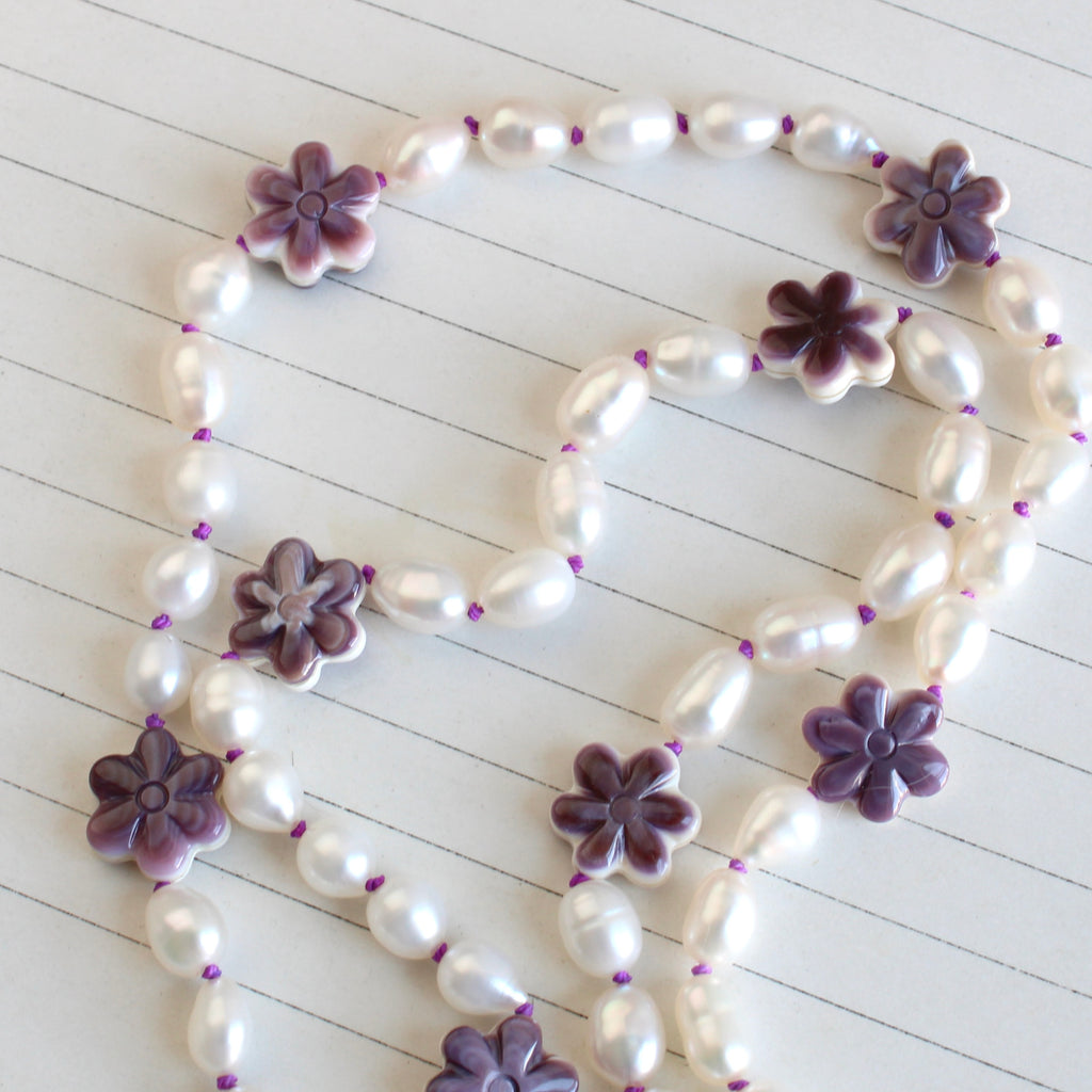 white oblong cultured pearls knotted on purple silk with spacers of carved purple and white shell flowers