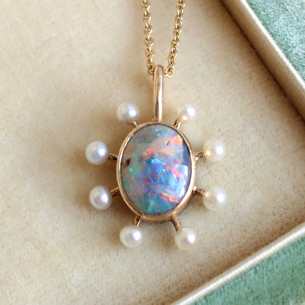 oval opal cabochon with intense colors in a gold bezel with little pearl studs around the outside