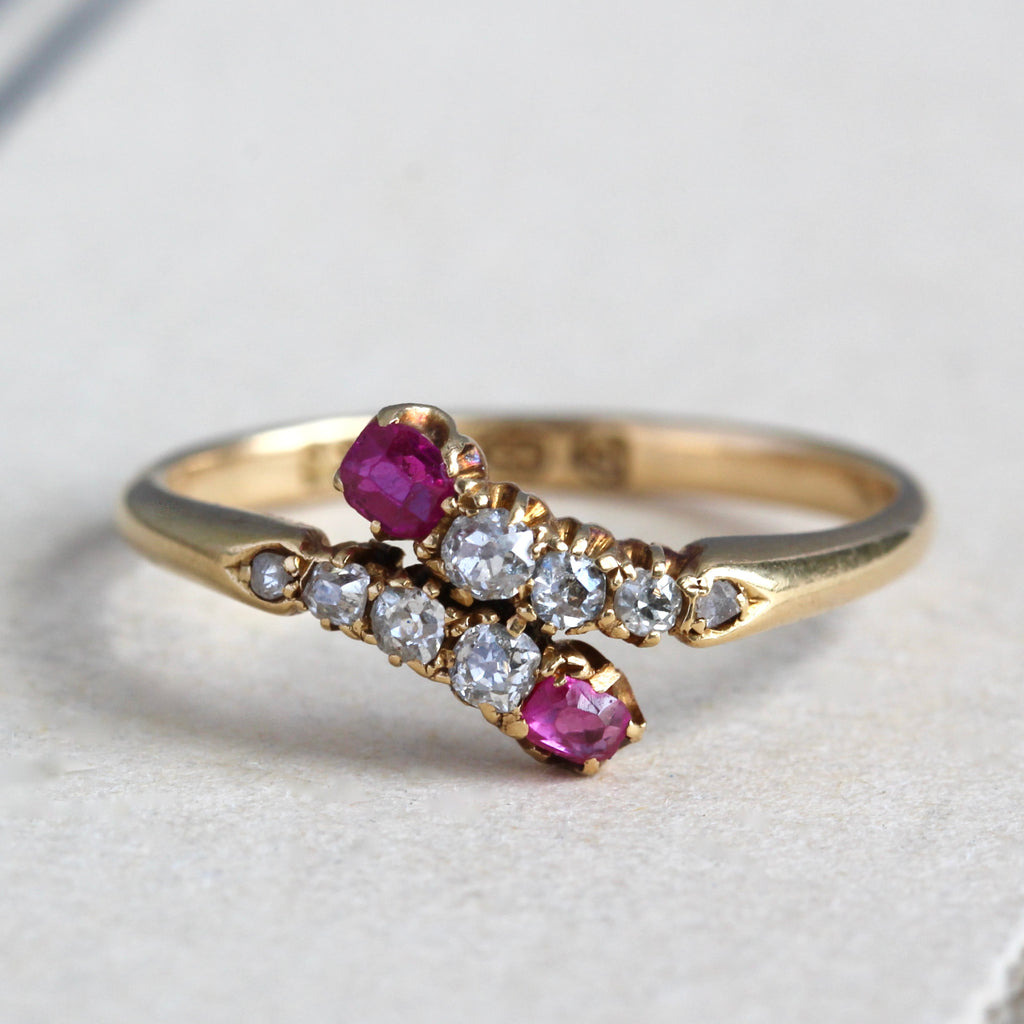 yellow gold ring with slim band and a crossover motif with diamonds accented by twin rubies