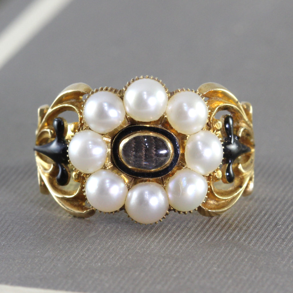 18k yellow gold ring with a pearl halo around the center which holds a memento of woven hair under crystal. Flanked by scroll detailing on the band.