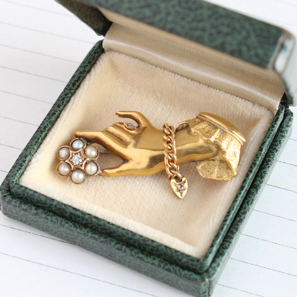 brooch designed as a gold hand wearing a bracelet and ring holding a flower