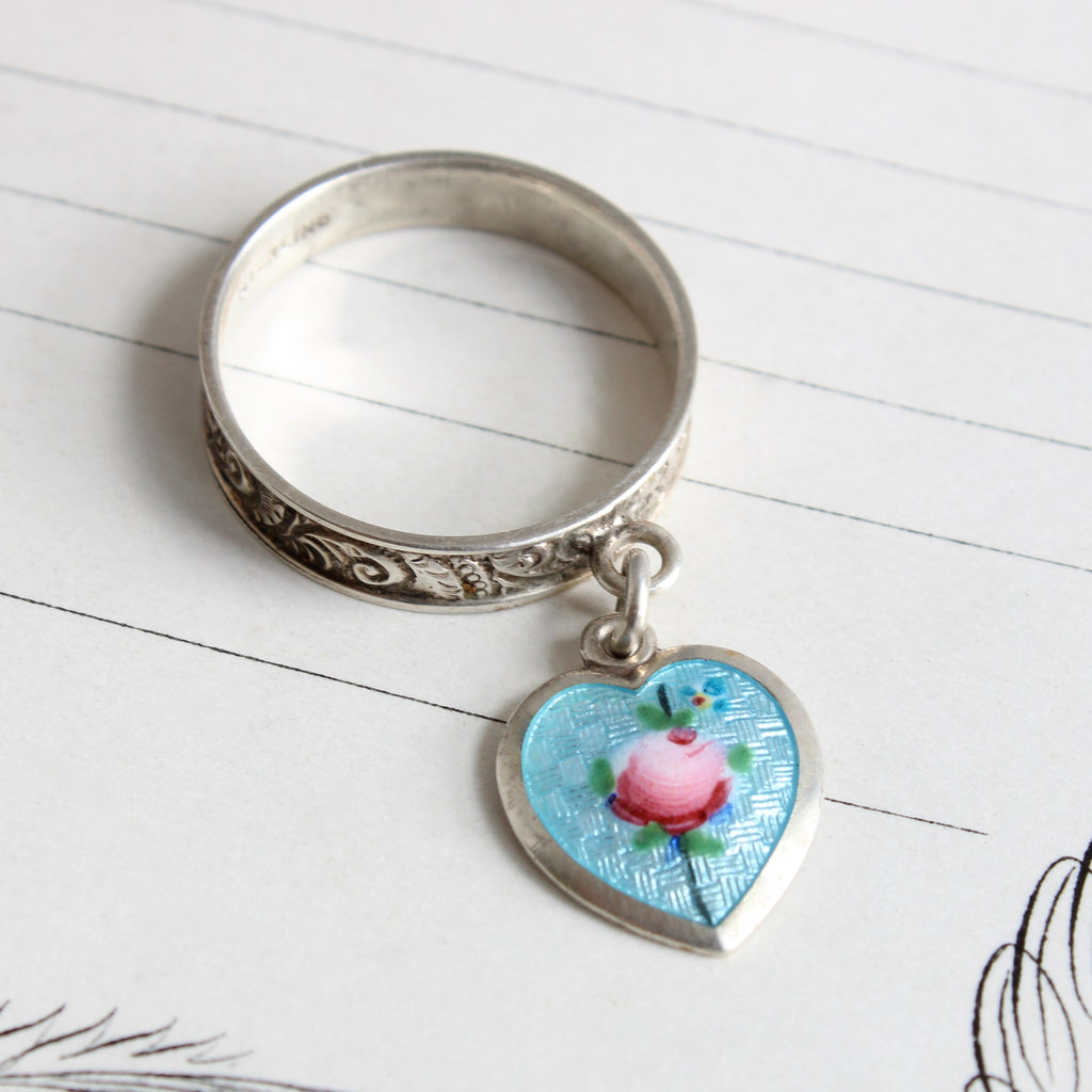 silver ring chased all around the band with a scroll pattern with an attached heart charm enameled blue with a pink rose