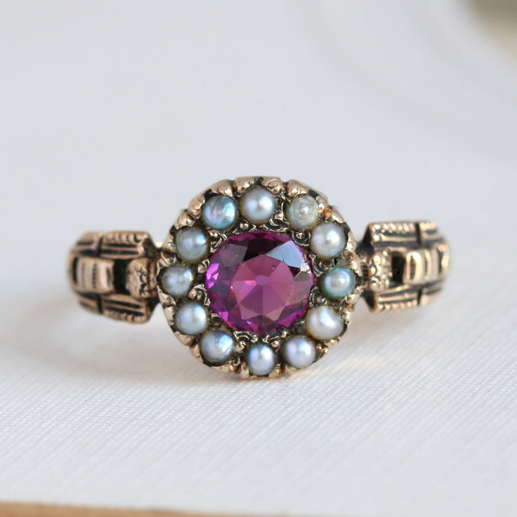 yellow gold ring with raspberry-red garnet that has a frame of natural pearls