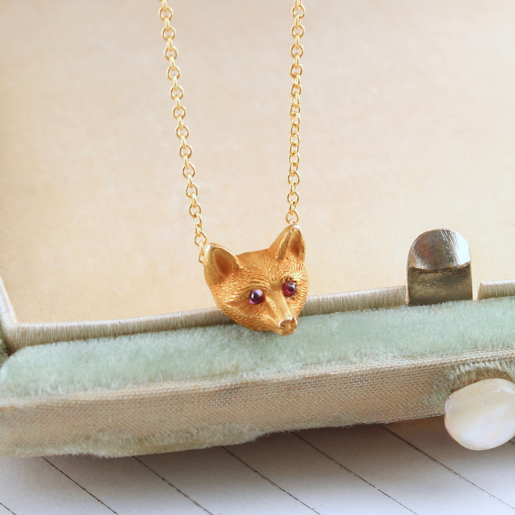 small golden fox head with garnet eyes attached to a gold chain as a necklace