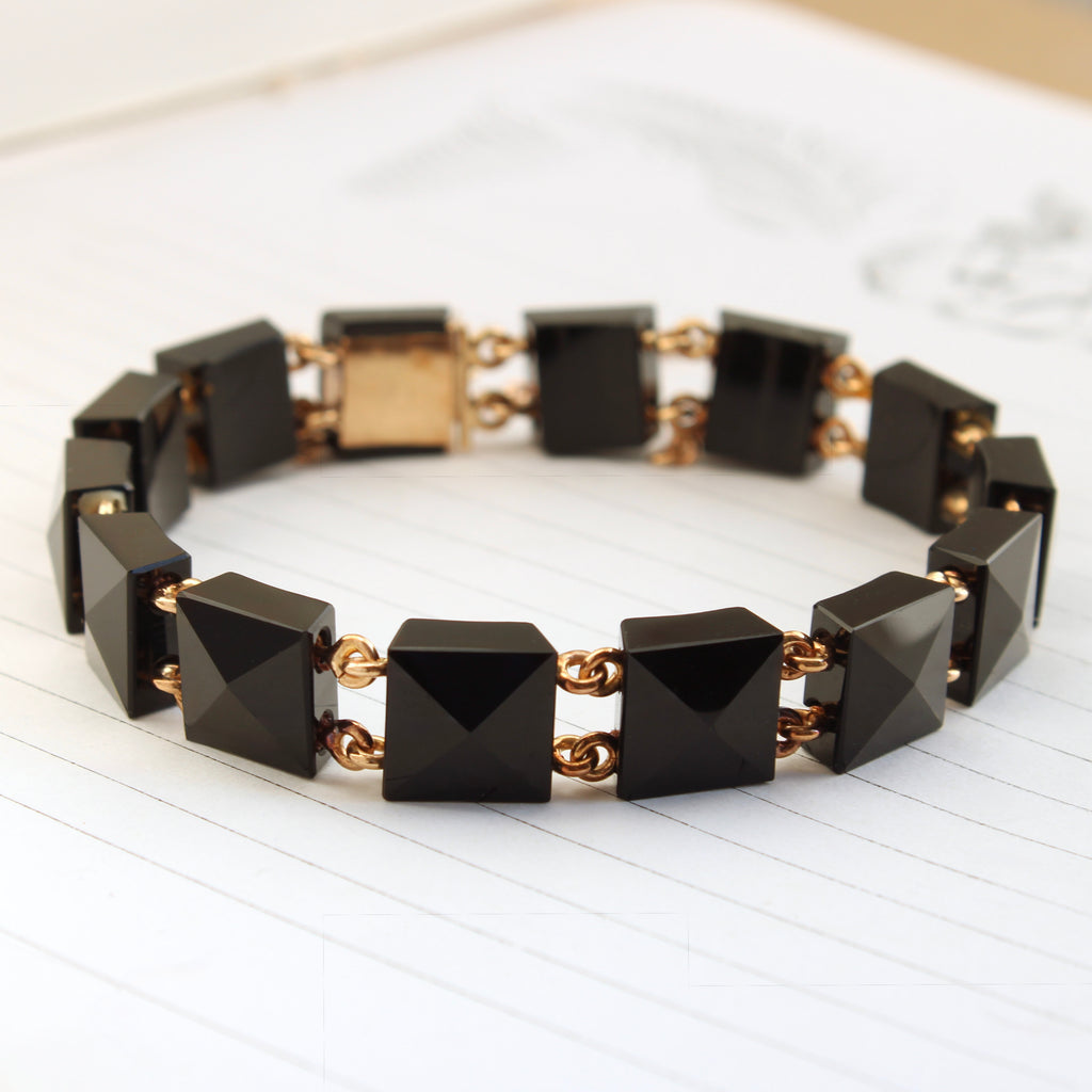 black squares with pyramid shaped tops connected by gold links as a bracelet