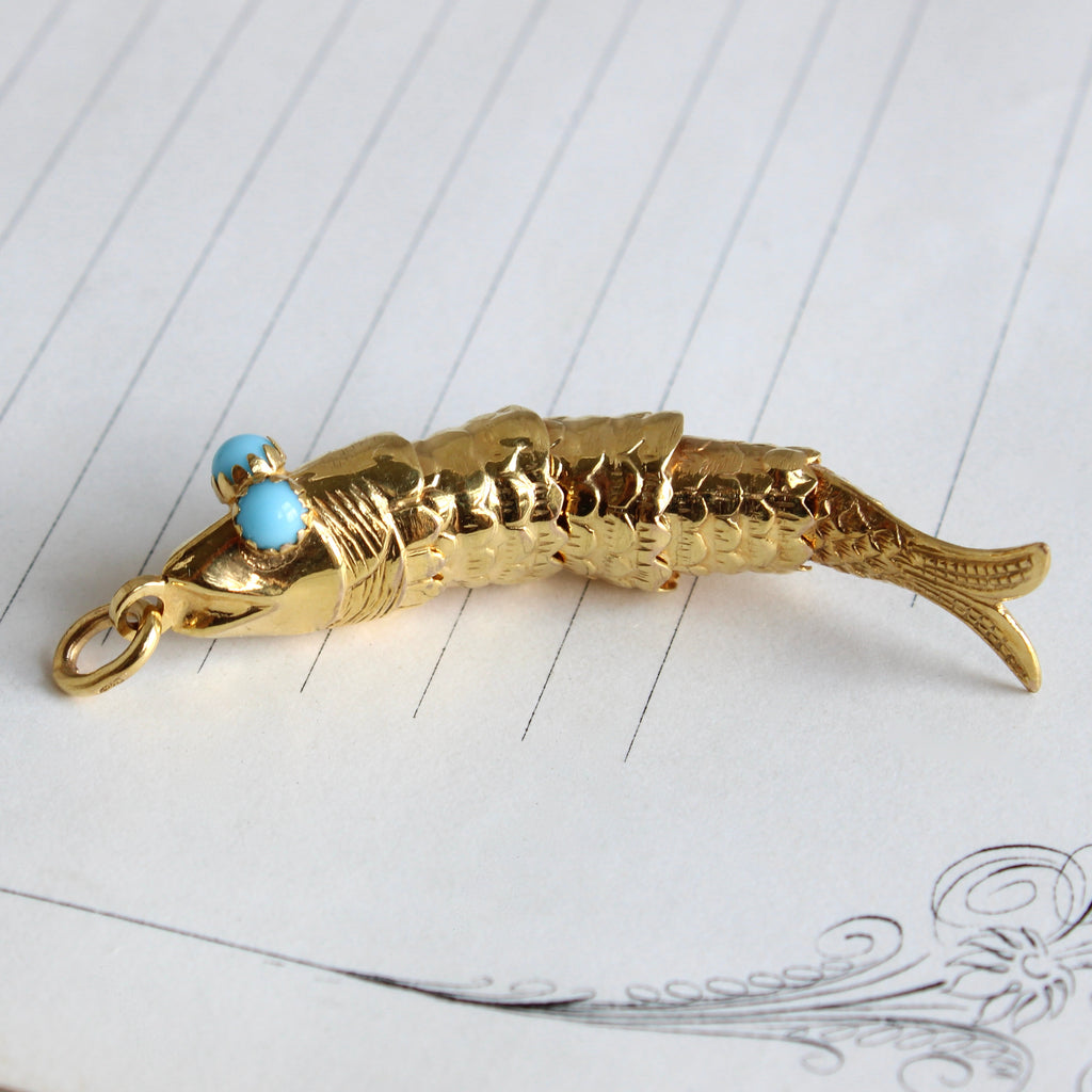 fish charm in yellow gold with blue turquoise eyes, designed in connected sections so it wiggles 