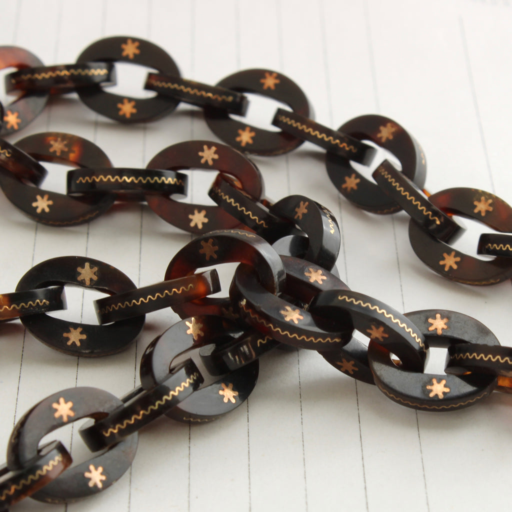 natural brown shell chain, the links inlaid with karat gold stars and a zigzag pattern along the edge