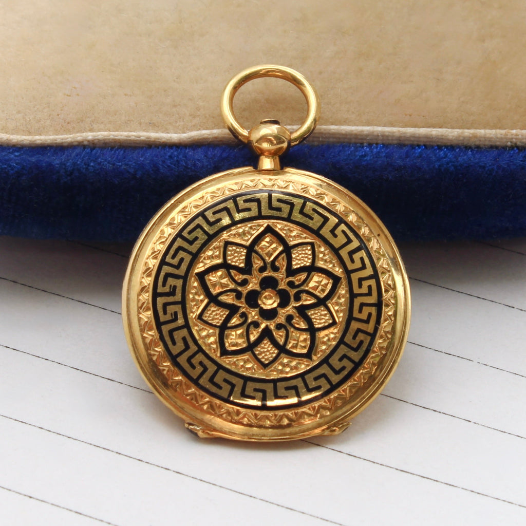 small round yellow gold locket with black enamel flower design and pattern bordering the edge