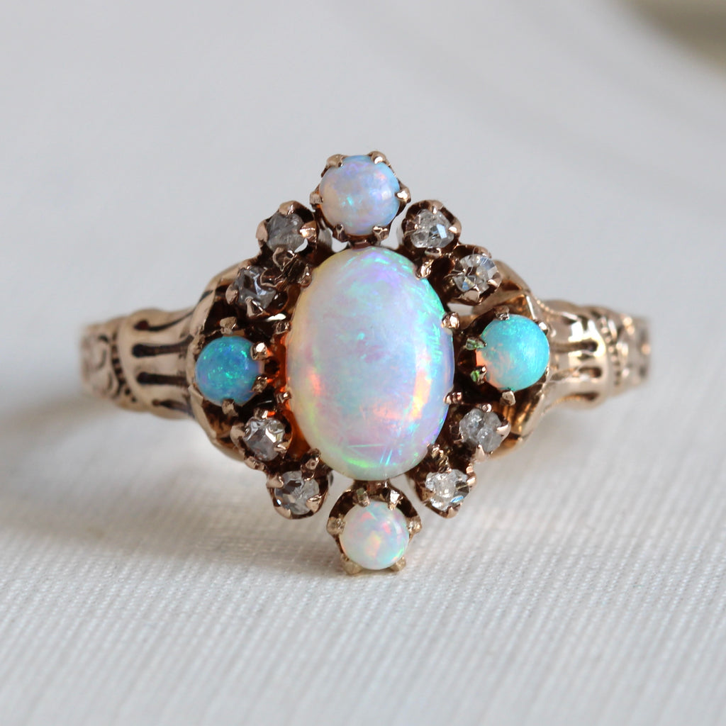 yellow gold ring with a central oval opal surrounded by rose cut diamonds and smaller opals