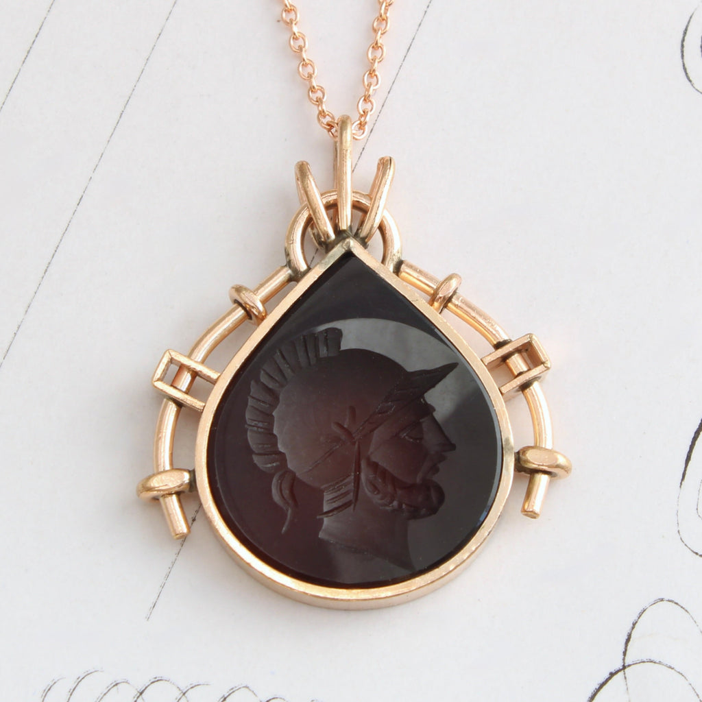 tear drop shaped reddish brown stone carved with the profile of a roman soldier in a gold metals bezel as a pendant