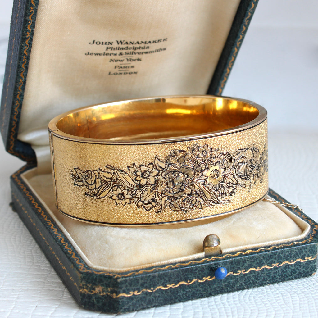 wide gold metal bangle with engraved flower decoration outlined in black enamel