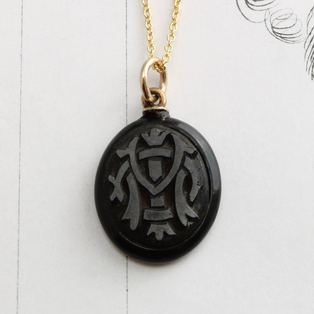 oval charm of shiny black natural material carved with the monogram IMO