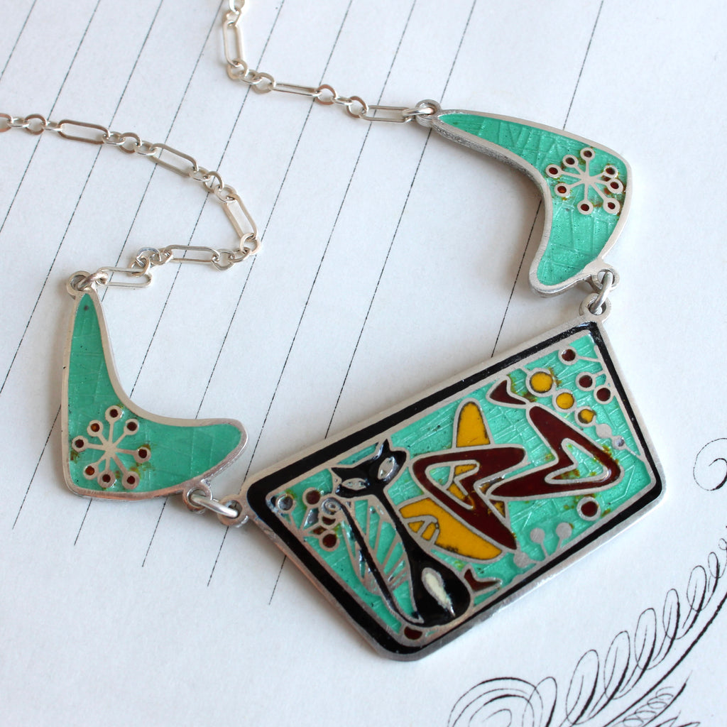 enamel silver necklace with a black cat against a turquoise backround filled with boomerang and bubble shapes