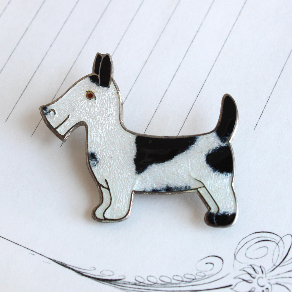 silver pin in the shape of a scottish terrier or scottie dog with black and white enamel