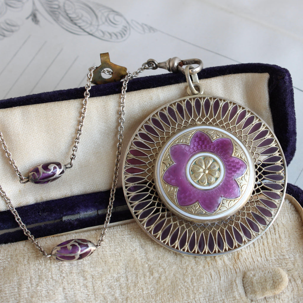 antique silver locket with a flower motif that has transparent purple enamel petals and a long silver chain