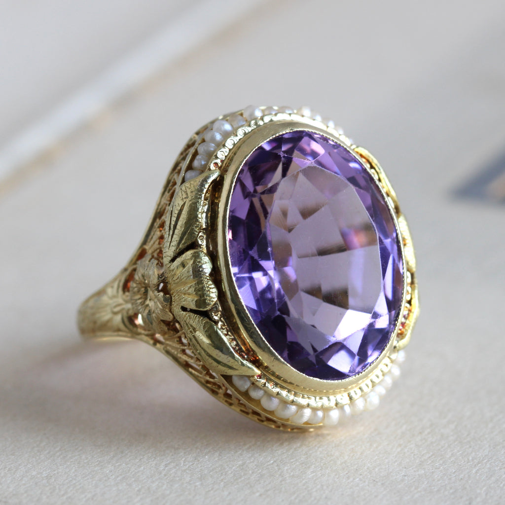 amethyst ring in lemon yellow gold filigree with flowers on the shoulders and halo of seed pearls around the stone