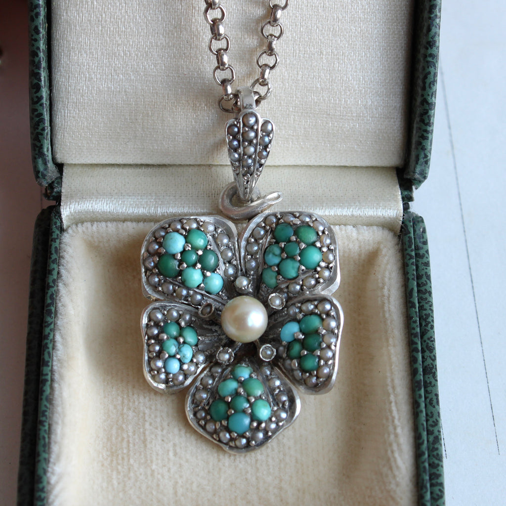 sterling pansey pendant closely set with small turquoise cabochons and seed pearls with a large round pearl in the center, on a silver chain