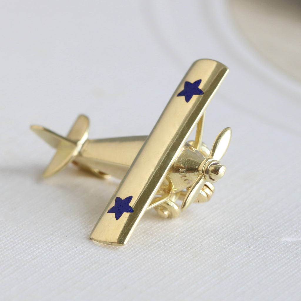 miniature single propeller plane pin in yellow gold with a blue star enameled on each wing.