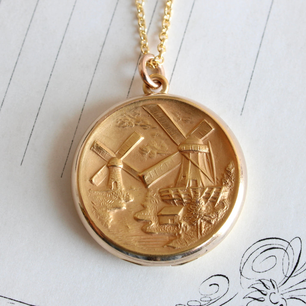 yellow gold locket embossed with a scene of windmills on a canal, hung on a gold chain