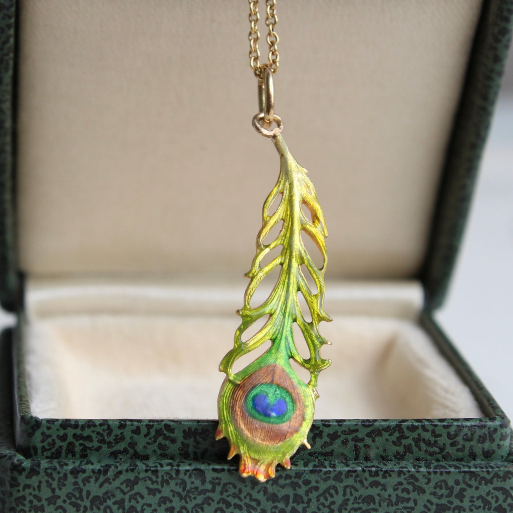 gold peacock feather charm enameled in greens and blues hung from a chain