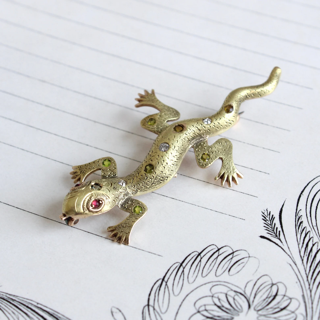 Antique yellow gold pin featuring a salamander lizard with garnet eyes and peridot and diamond set along his back and legs. 