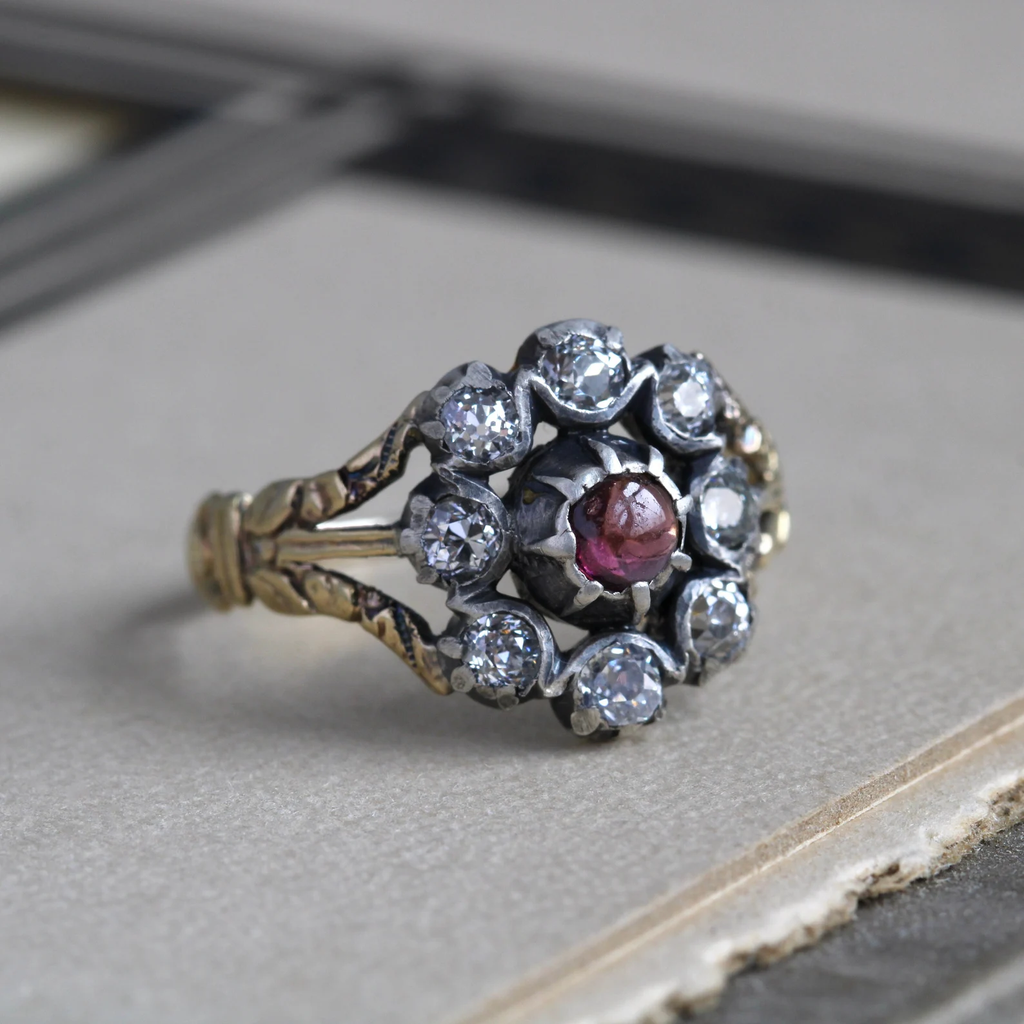 Antique yellow gold ring with a garnet cabochon surrounded by a halo of eight sparkling diamonds in silver cup bezels.