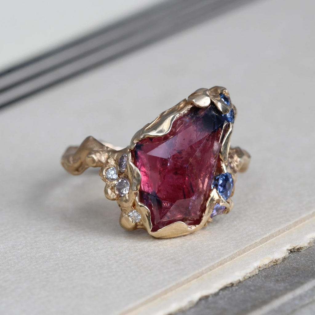 Handmade yellow gold ring with a faceted ruby surrounded by blue tanzanite stones and natural diamonds in a hammered style bezel and band