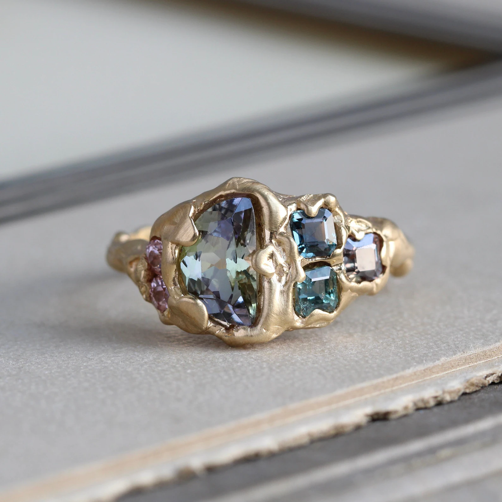 Handmade yellow gold ring with a faceted half moon bi-color tanzanite surrounded by tanzanite, spinel, and garnet stones in a hammered style bezel and band.