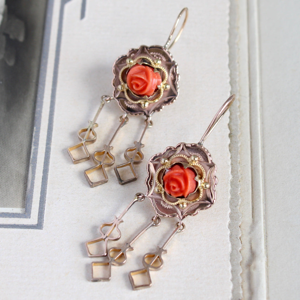 Antique yellow gold dangle earrings with carved red coral rose buds in ornate bezels and hanging charms.