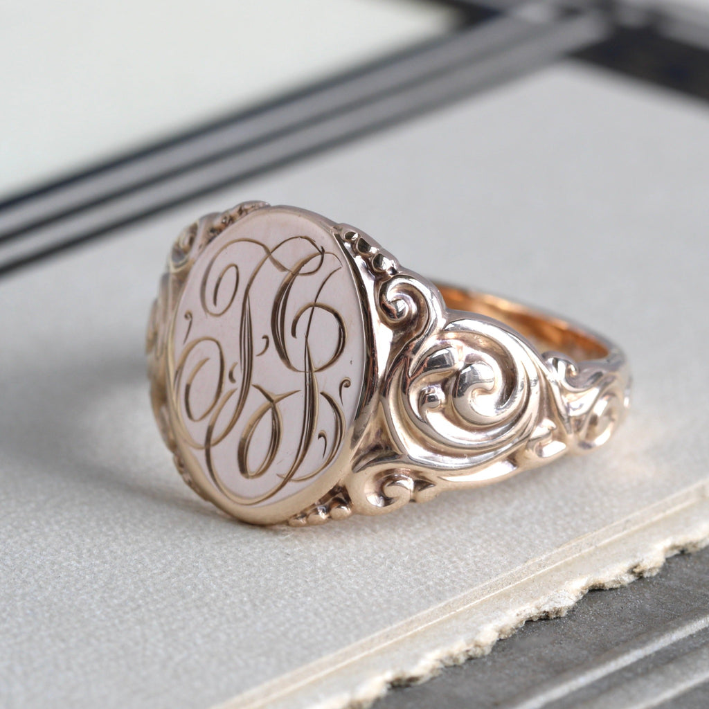 antique rose gold signet ring with scroll designs on band and initials on front.