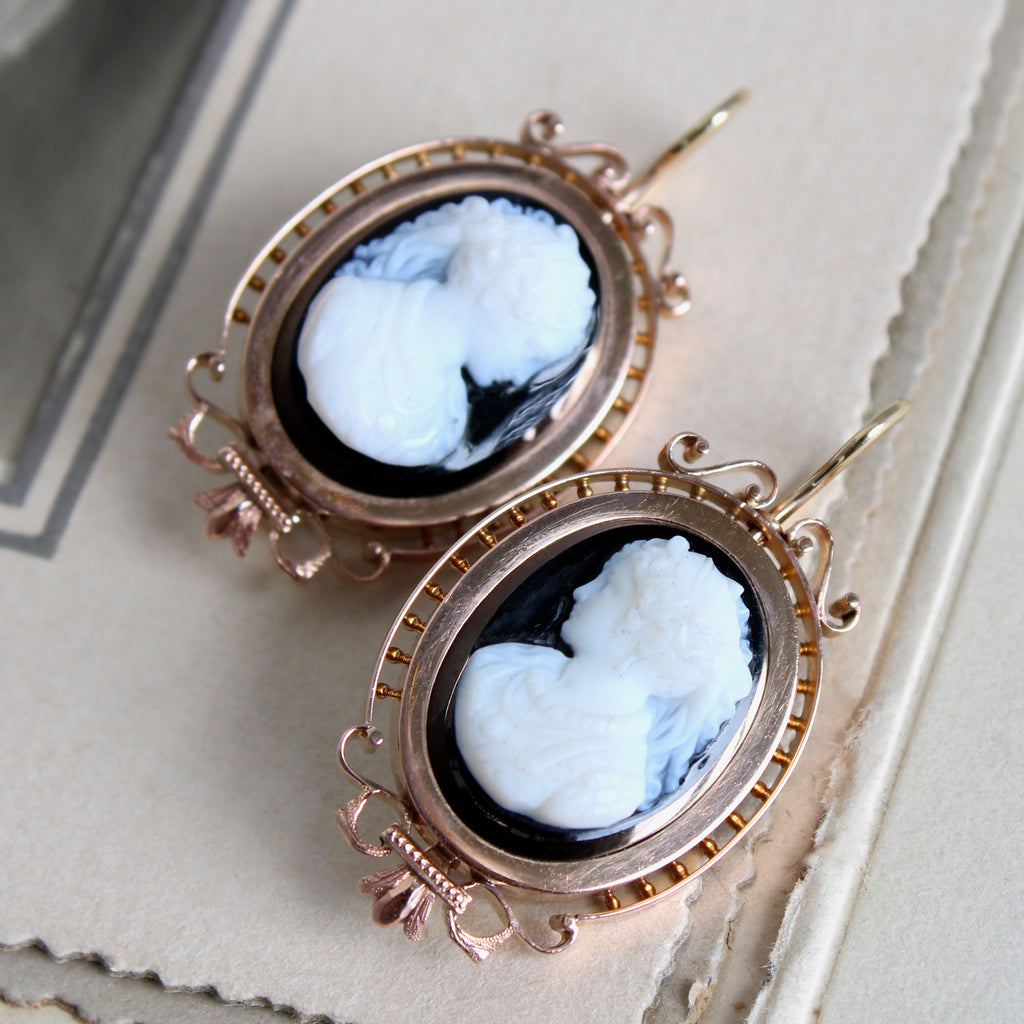 Antique gold earrings with carved black and white cameos in ornate bezels and wire hook backs.