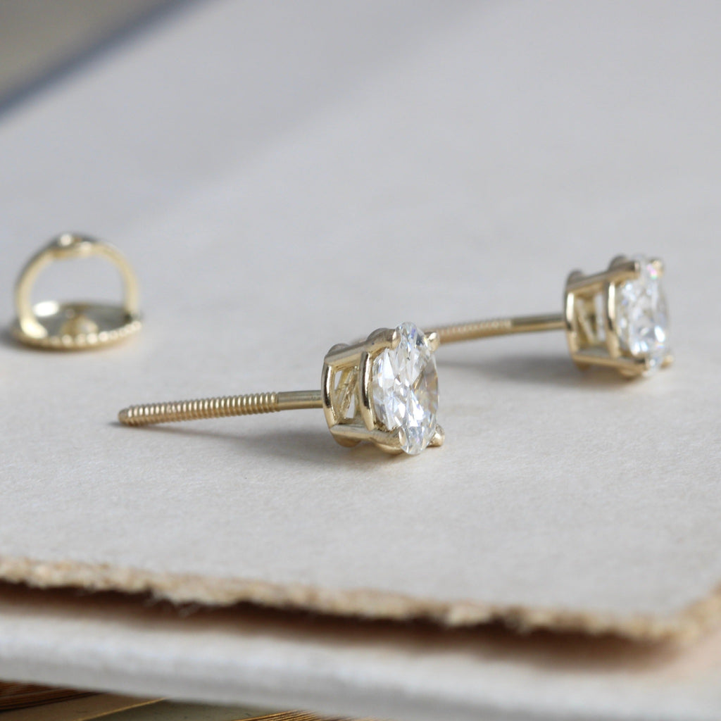 side view of a pair of white diamond stud earrings in yellow gold 4-prong settings and threaded posts
