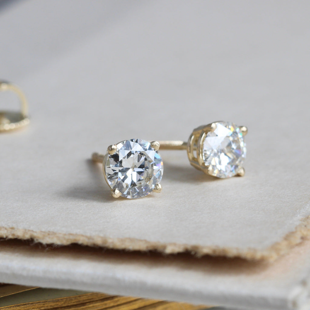 3/4 view of a pair of bright white diamond stud earrings in yellow gold 4-prong settings and screw-back posts